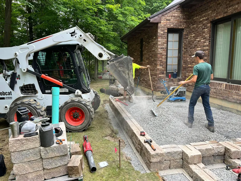 A man is working on a patio in front of a bobcat.