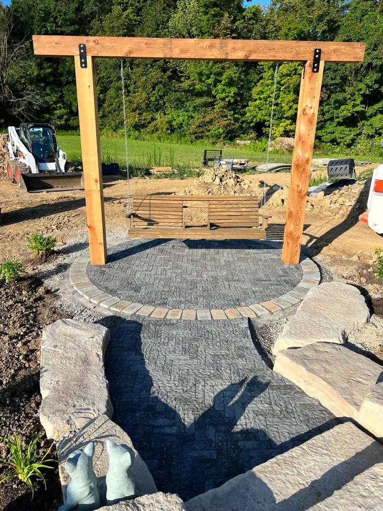 A wooden swing is sitting in the middle of a stone patio.