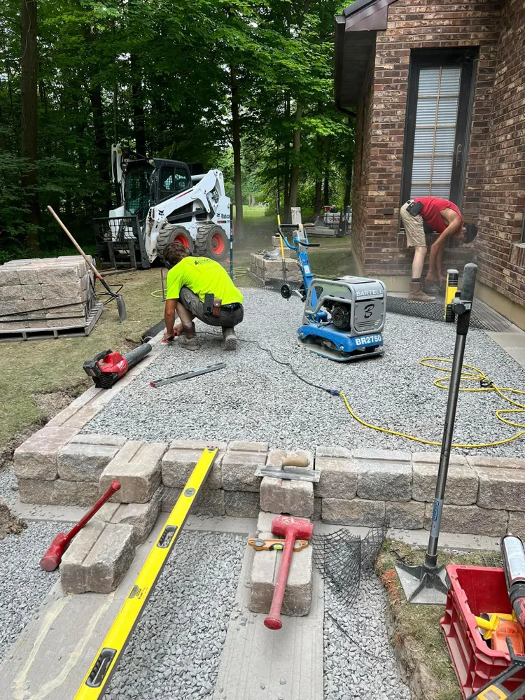 A group of construction workers are working on a driveway in front of a brick house.