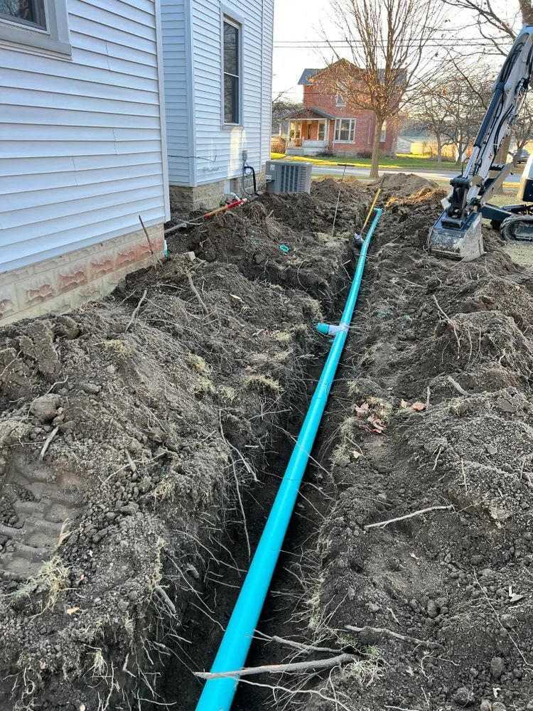 A blue pipe is being installed in the dirt next to a house.