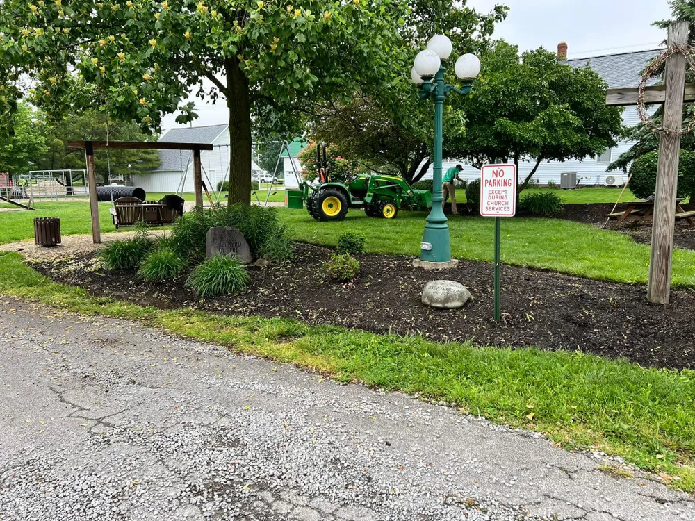 A green tractor is parked in a grassy area next to a street light.