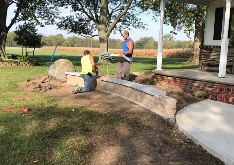 Two men are working on a brick wall in front of a house.