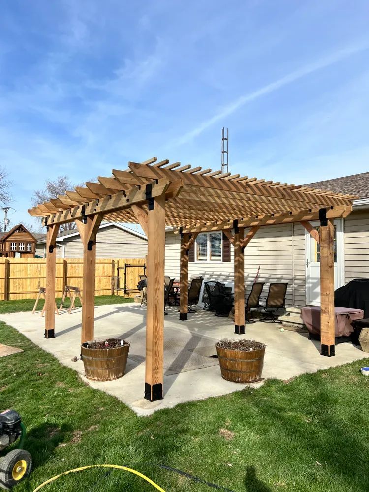 A wooden pergola is sitting on top of a concrete patio in a backyard.