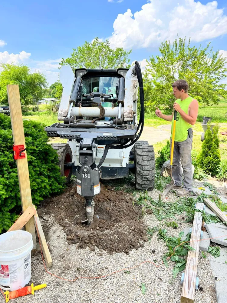 A man is standing next to a bulldozer digging a hole in the ground.
