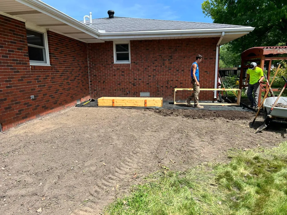 A group of men are working on a driveway in front of a brick house.
