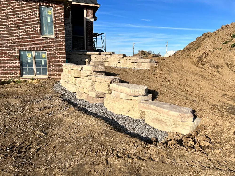 A stone wall is being built in front of a brick house.