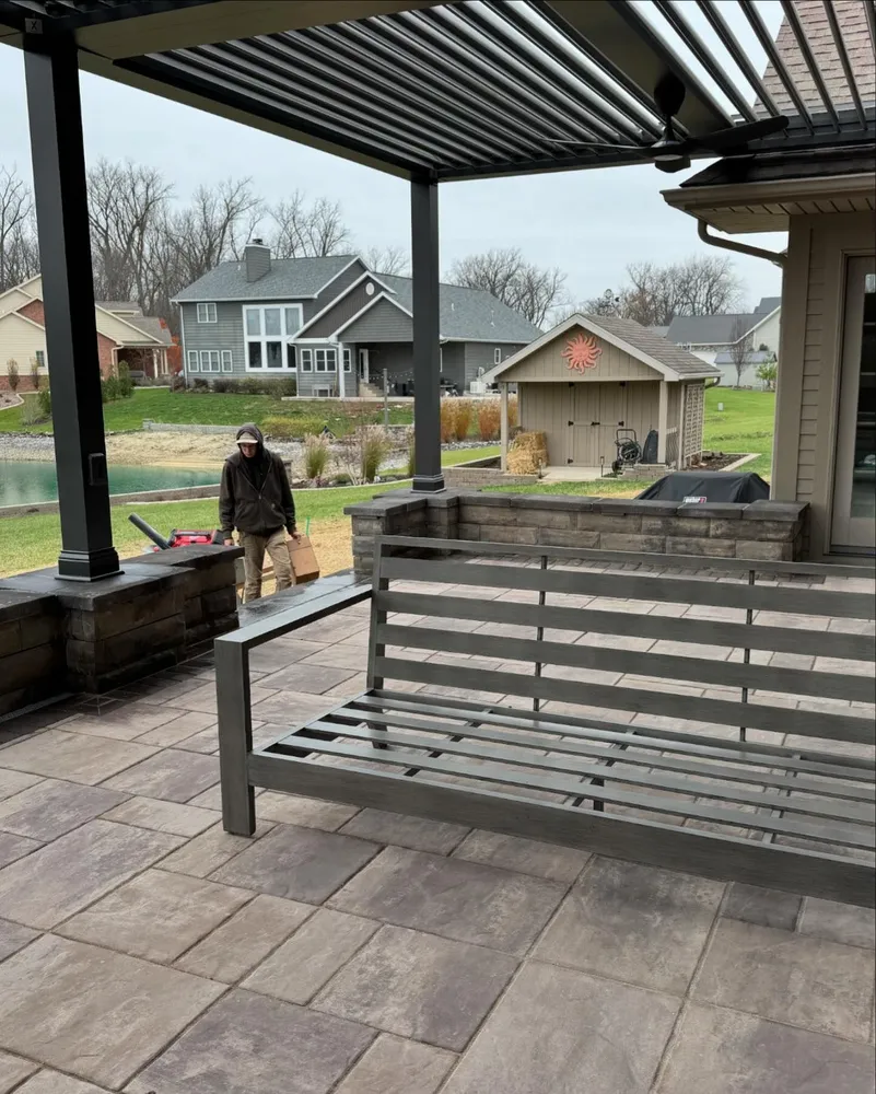 A man is standing under a pergola on a patio next to a swing.