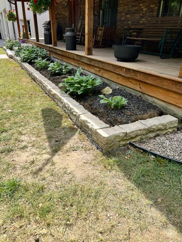 A planter filled with plants is in front of a house.