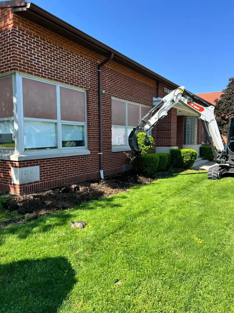 An excavator is digging in front of a brick building.