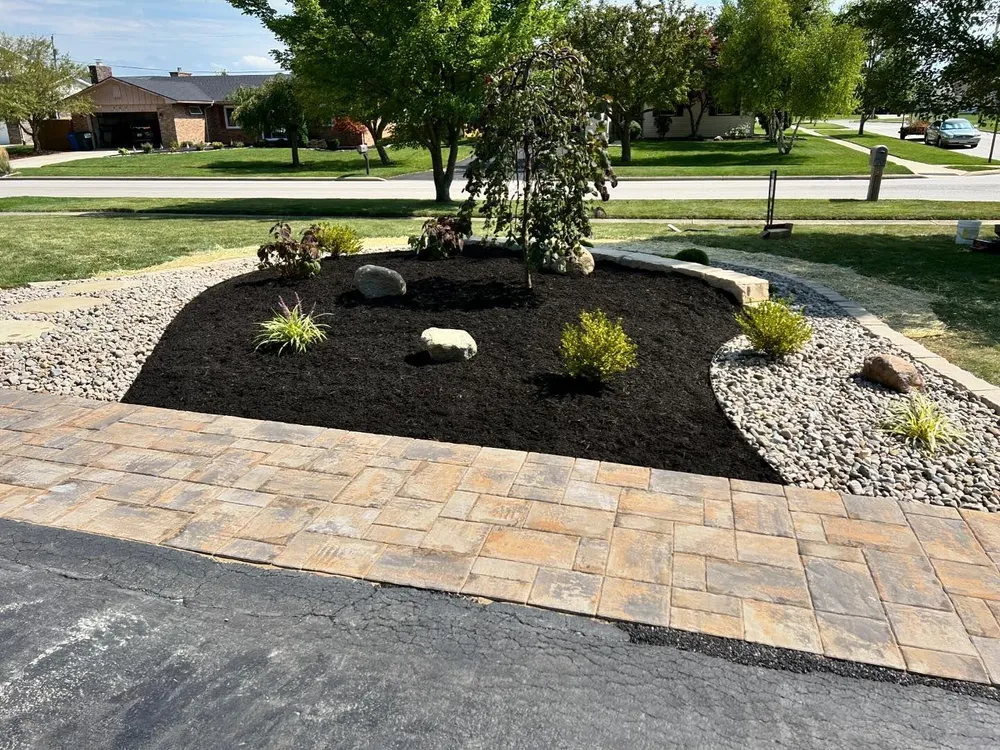 A driveway with a brick walkway and a garden in the middle of it.
