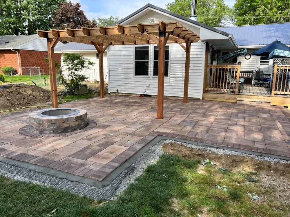 A patio with a fire pit and a pergola in front of a house.