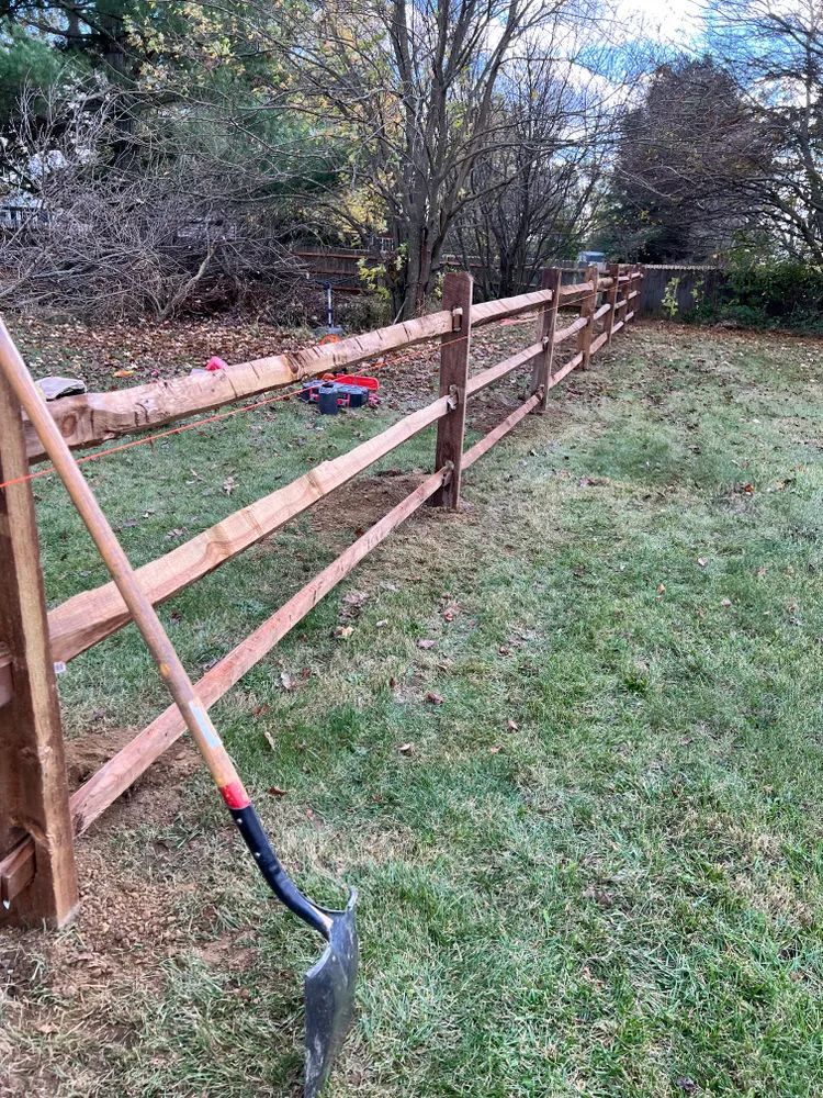 A shovel is sitting in the grass next to a wooden fence.