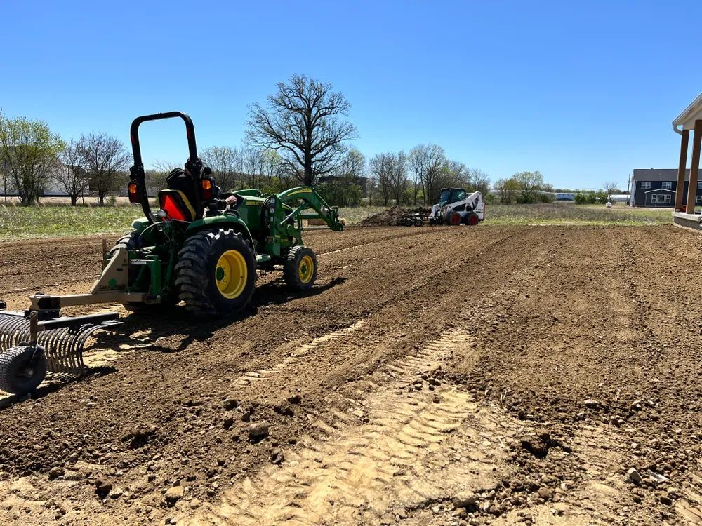 A green tractor is plowing a dirt field.