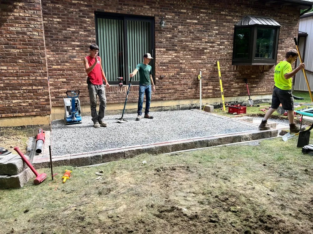 A group of men are working on a patio in front of a brick house.