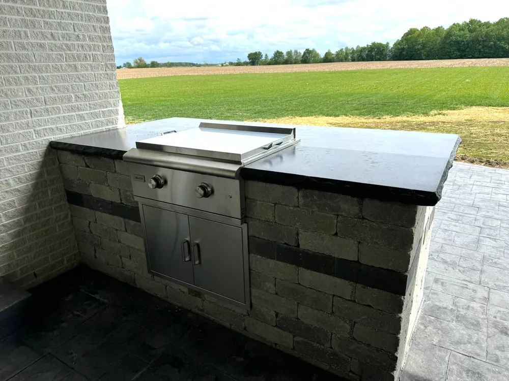 A grill is sitting on top of a counter next to a brick wall.