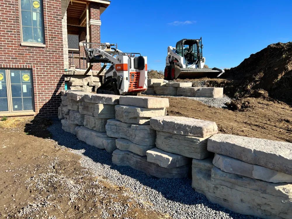A bulldozer is working on a stone wall in front of a brick house.