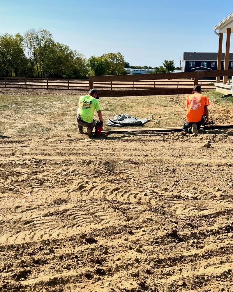 Two men are kneeling in the dirt in a field.