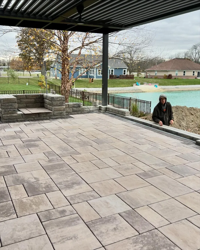 A man is standing on a patio next to a pool.