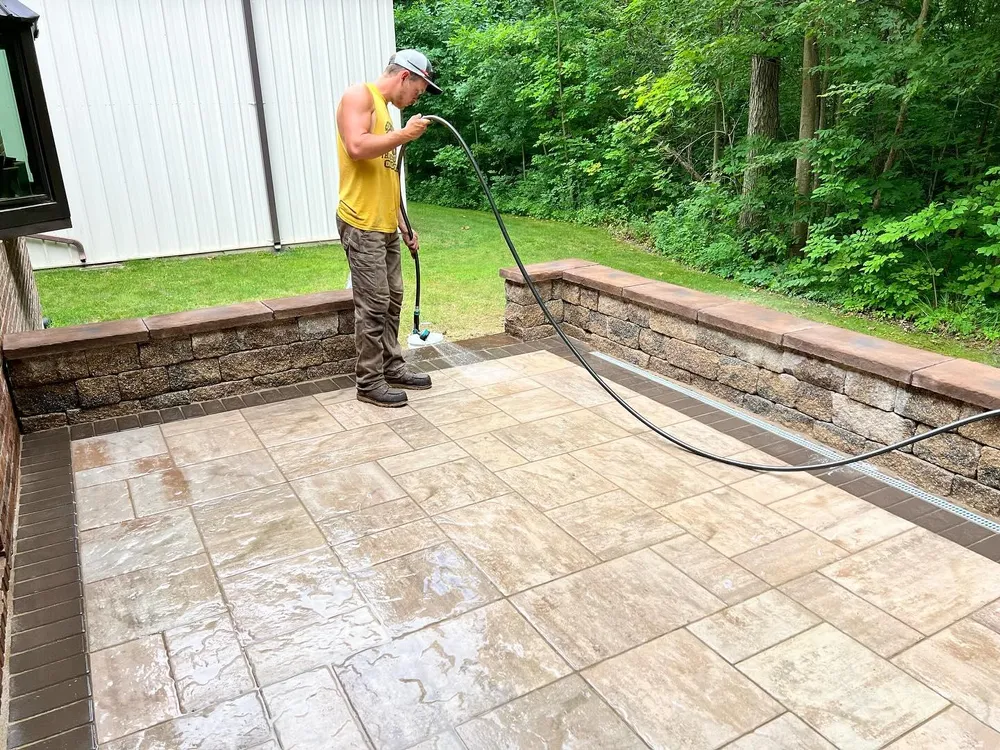 A man is cleaning a patio with a hose.
