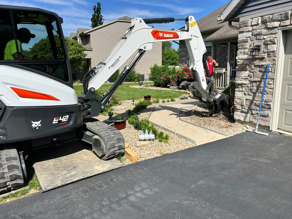 A small excavator is parked in a driveway in front of a house.