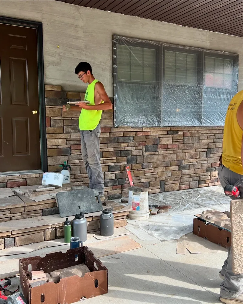 A man in a yellow vest is working on a stone wall