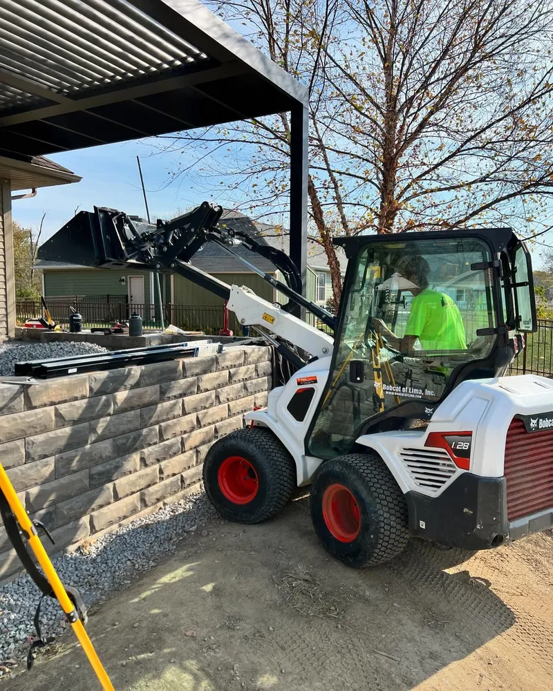 A man is driving a bulldozer next to a brick wall.