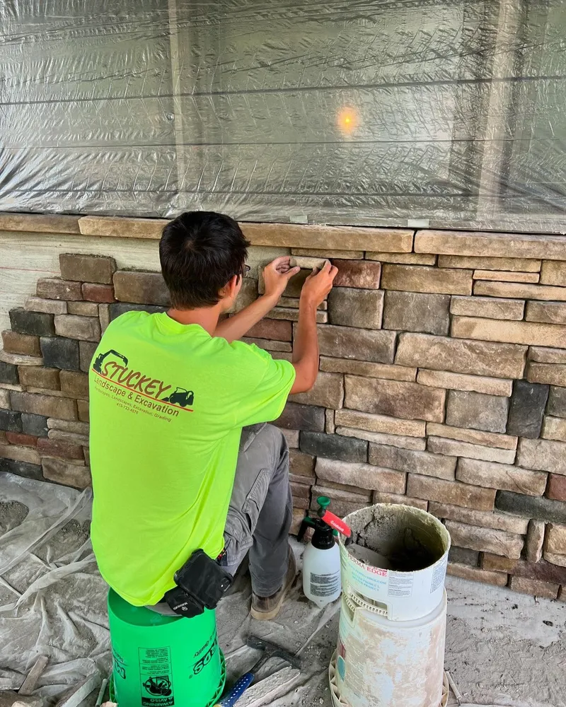 A man in a neon green shirt is working on a stone wall.