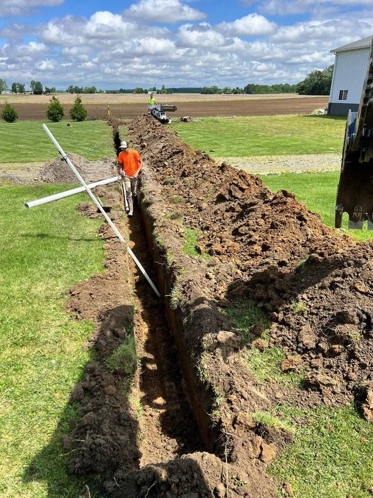 A man is digging a trench in the dirt in a field.