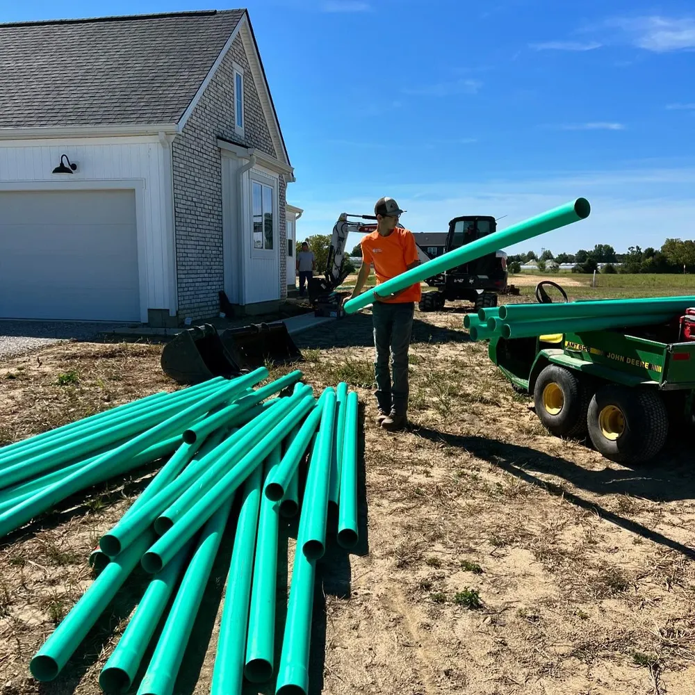 A man is holding a green pipe in front of a house