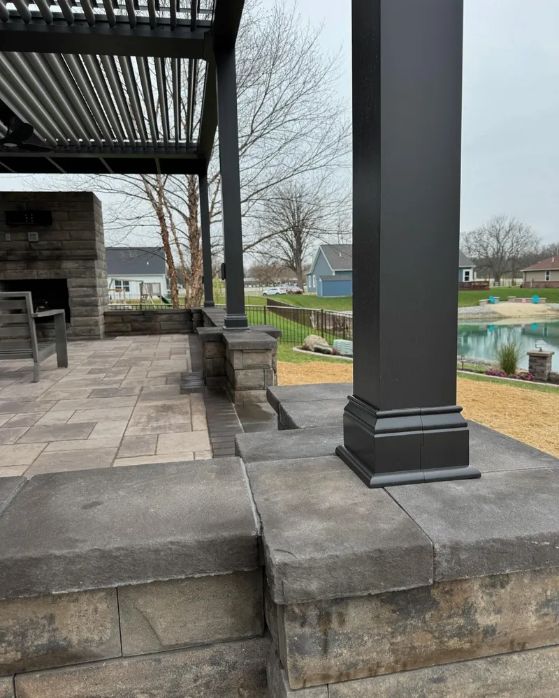 A patio with a pergola and a fireplace in the background.