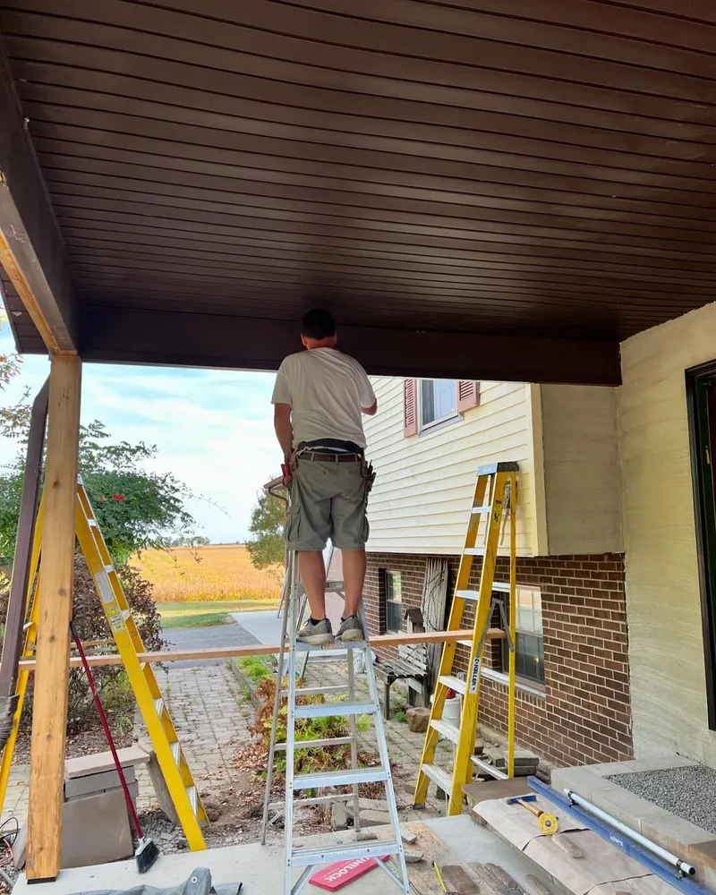 A man is standing on a ladder painting the ceiling of a house.