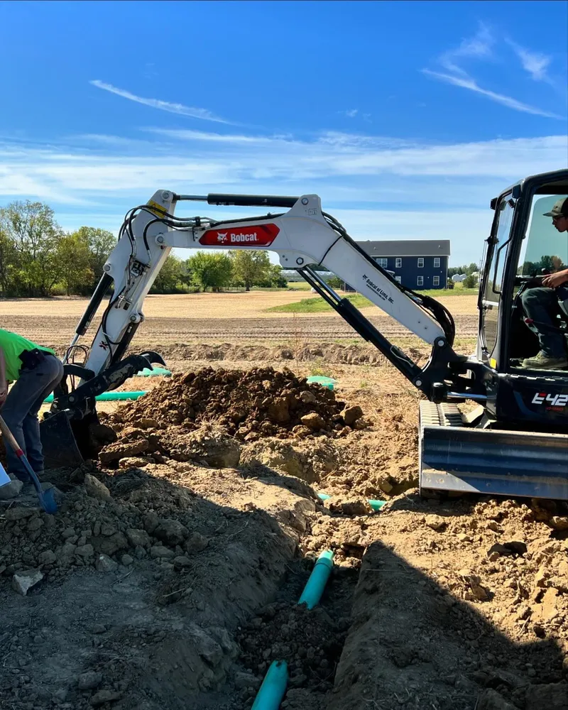 A man is digging in the dirt next to a bobcat excavator.