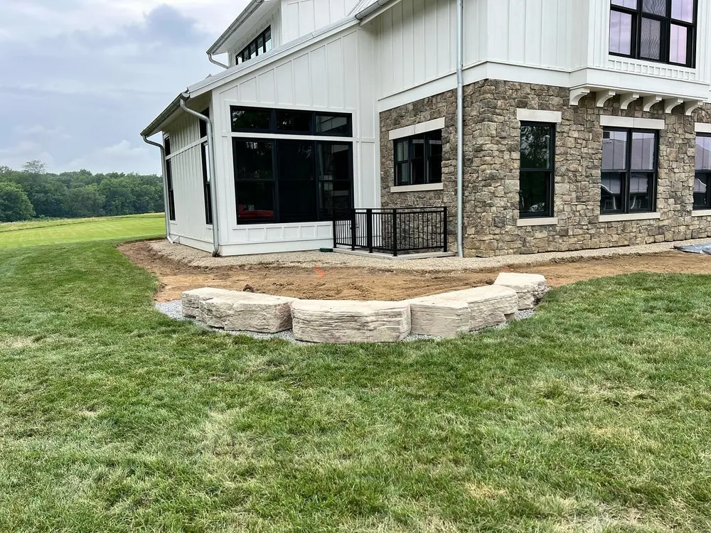 A large white house with a stone facade is sitting on top of a lush green field.