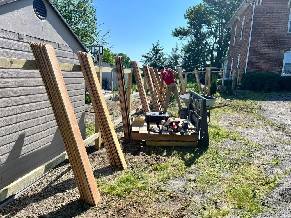 A man is working on a wooden fence in front of a house.