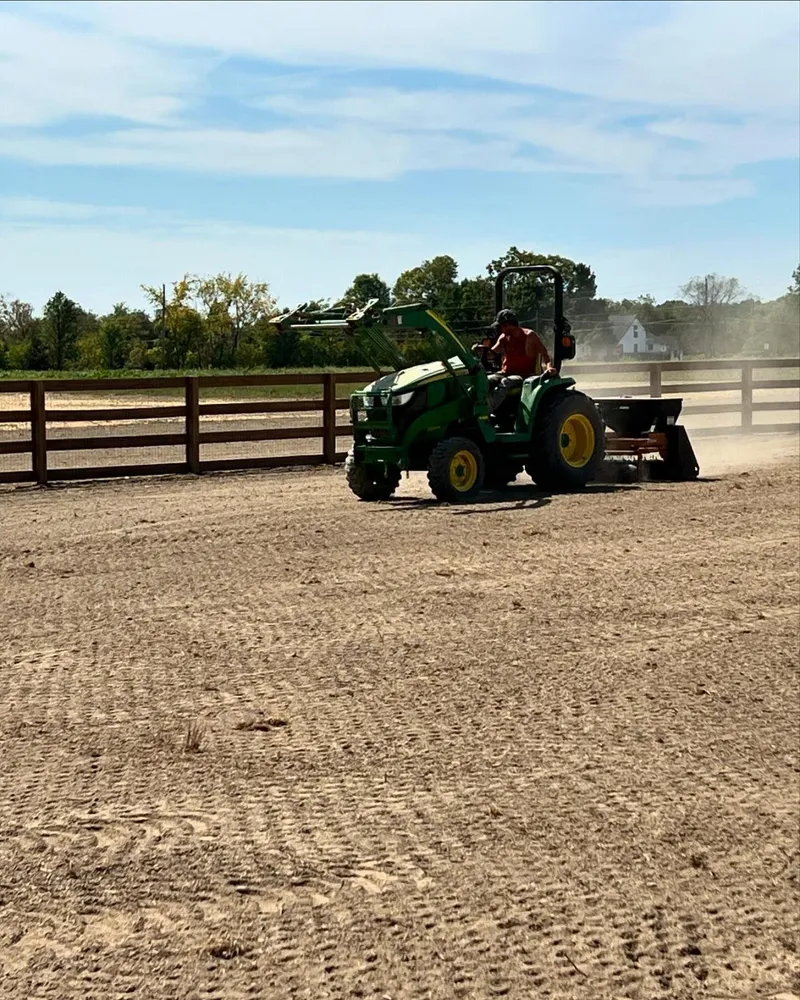 A man is driving a green tractor on a dirt field.