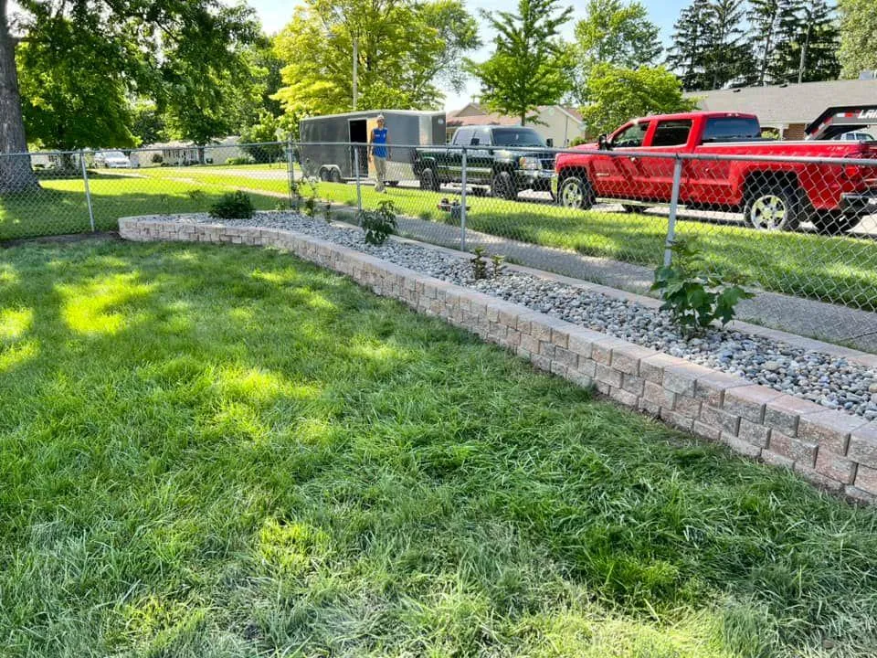 A red truck is parked in the grass next to a stone wall.