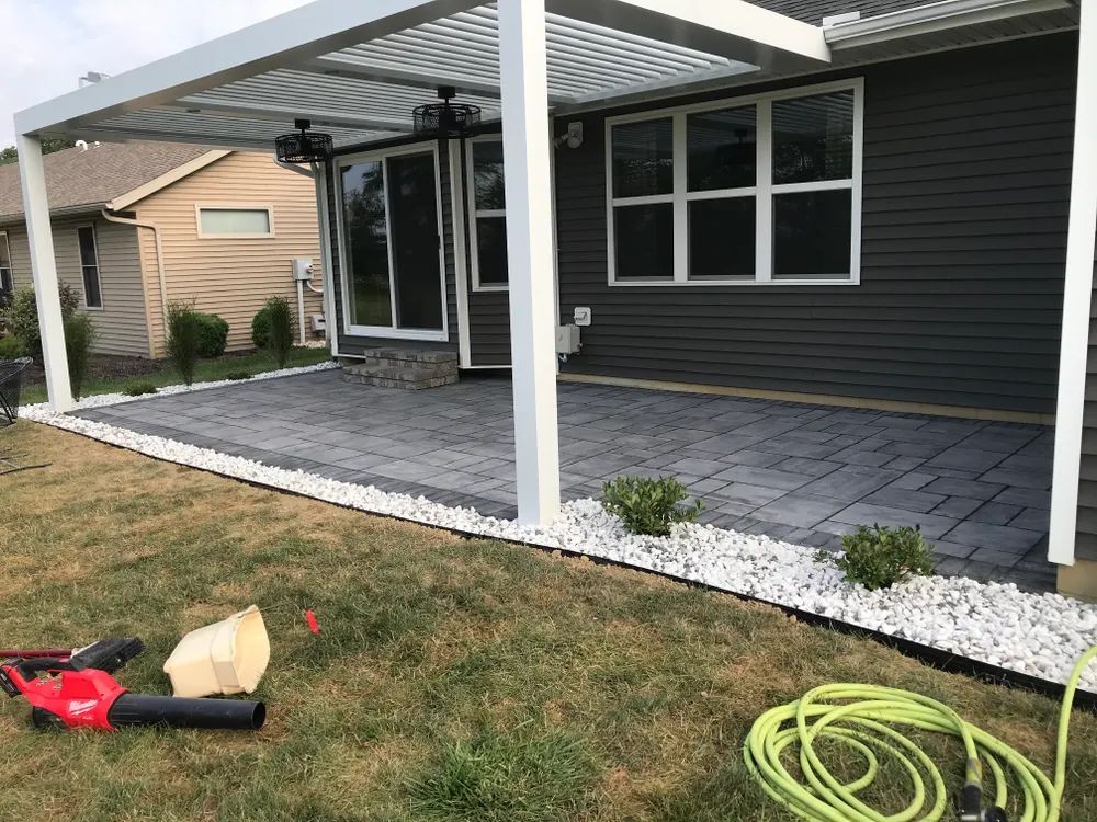 A patio with a pergola and a hose in front of a house.