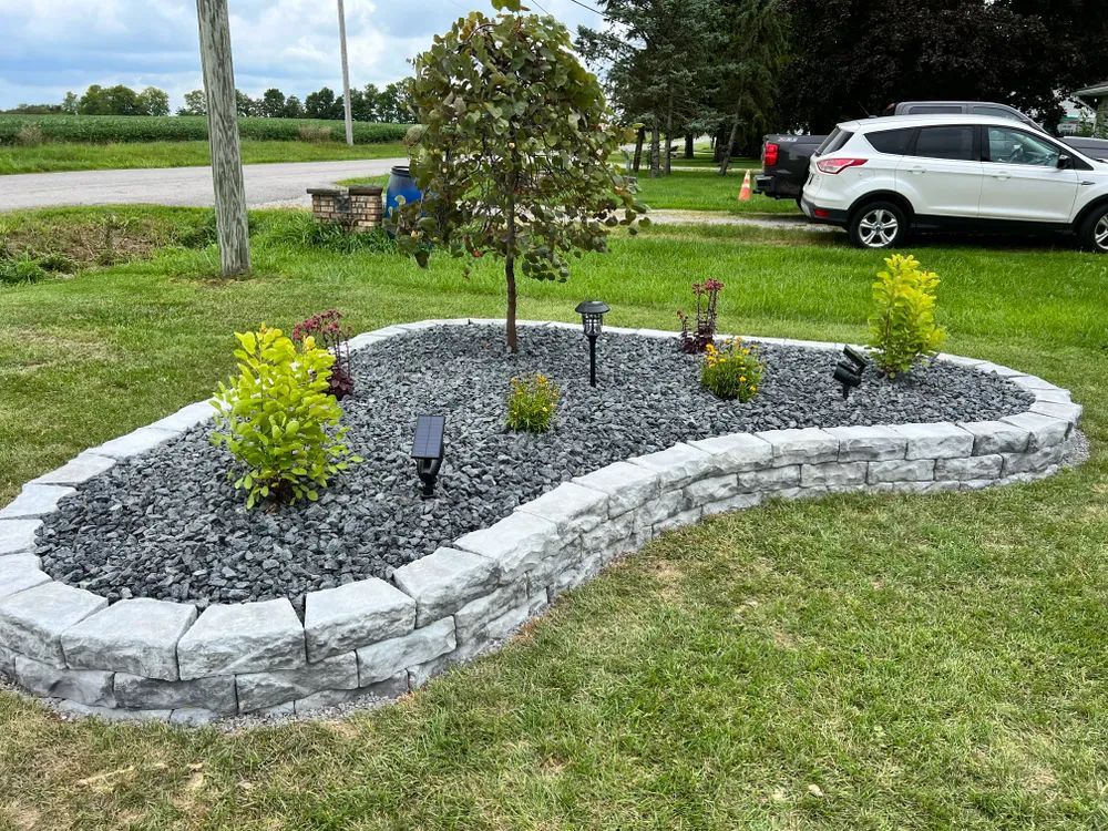 A large planter filled with rocks and plants in a yard with a car parked in the background.