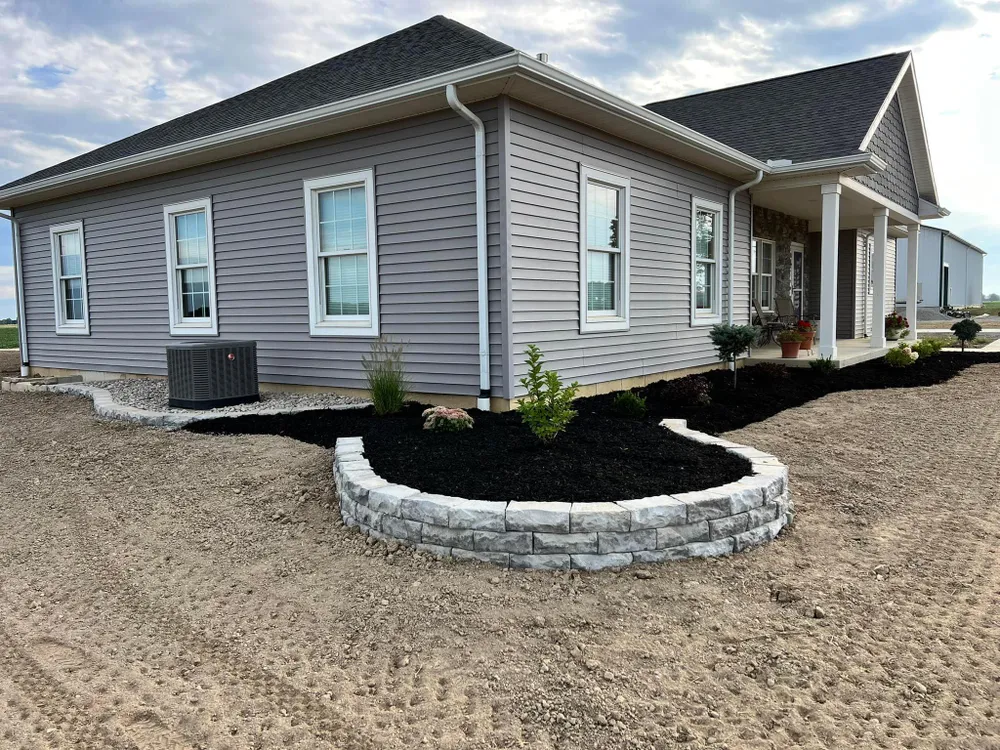 A large gray house with a black roof is sitting on top of a dirt field.
