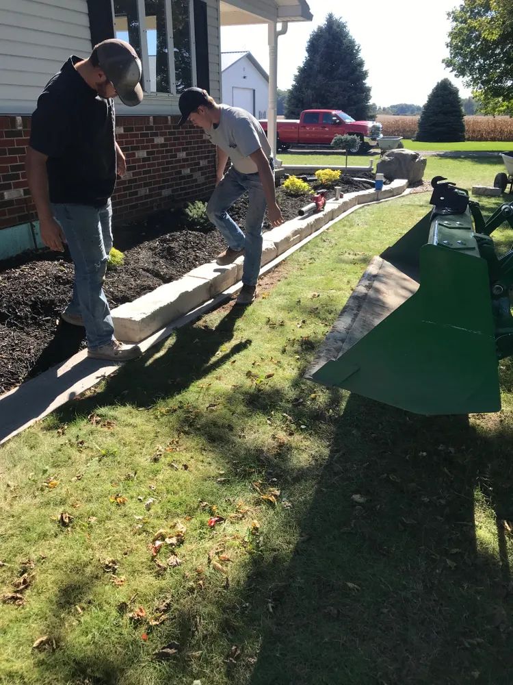 Two men are working on a sidewalk in front of a house