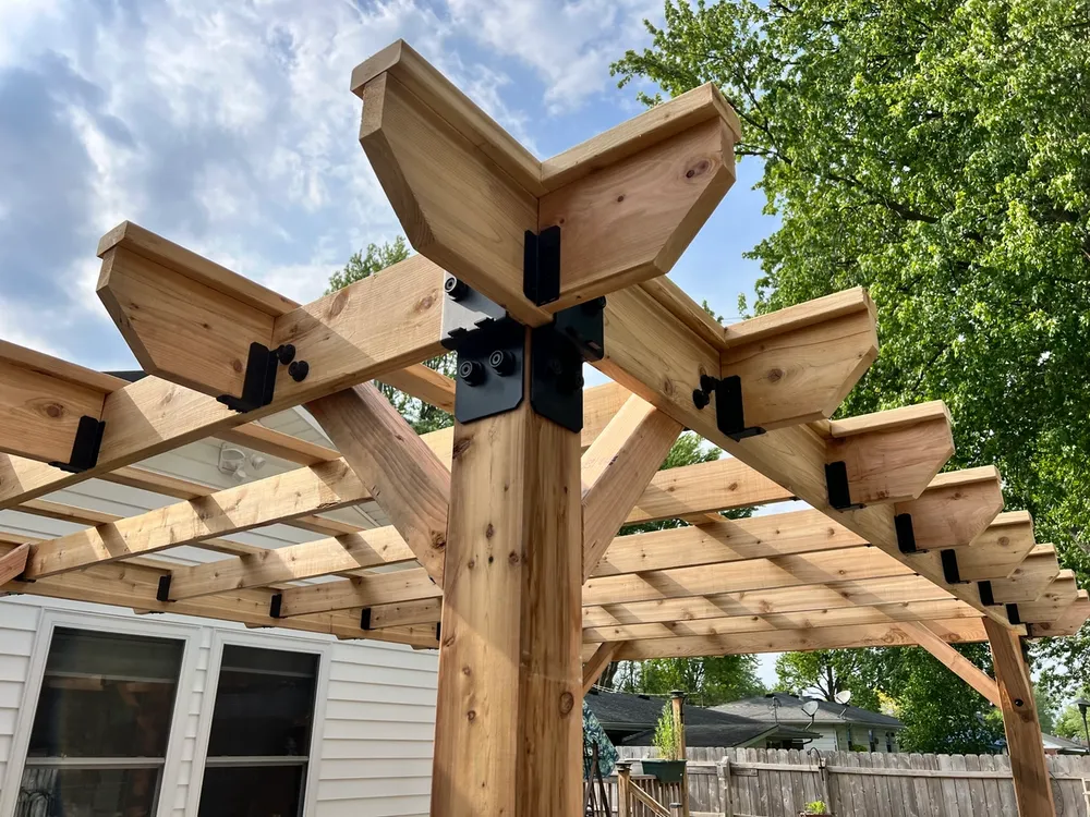 A wooden pergola is sitting in front of a white house.