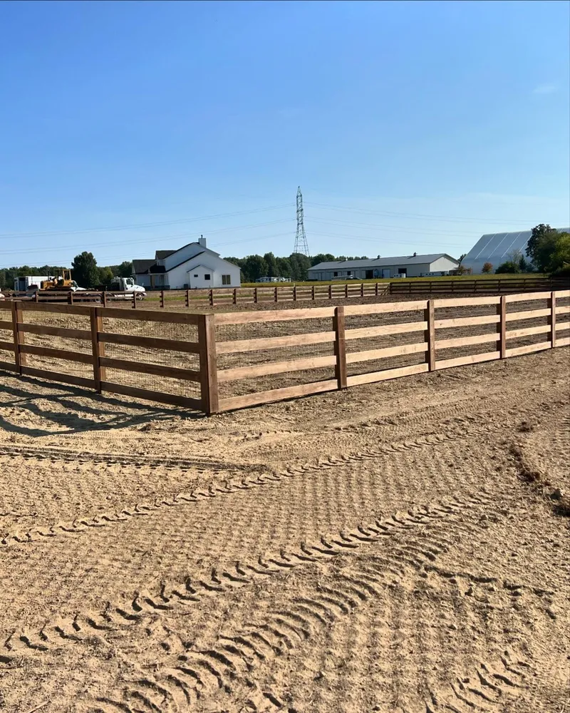A wooden fence surrounds a dirt field with a house in the background.