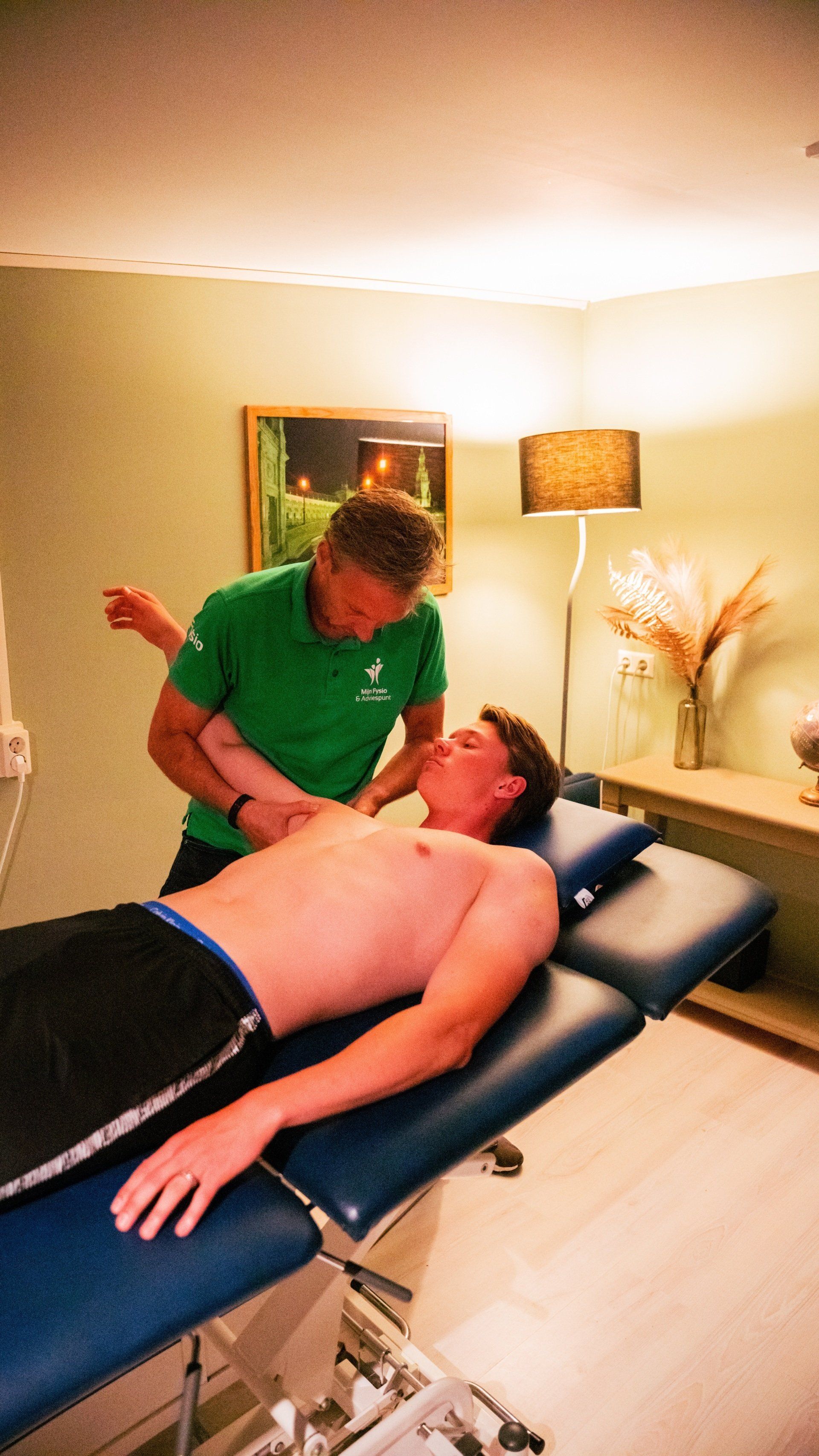 Een man ligt op een tafel en krijgt een massage van een man in een groen shirt.