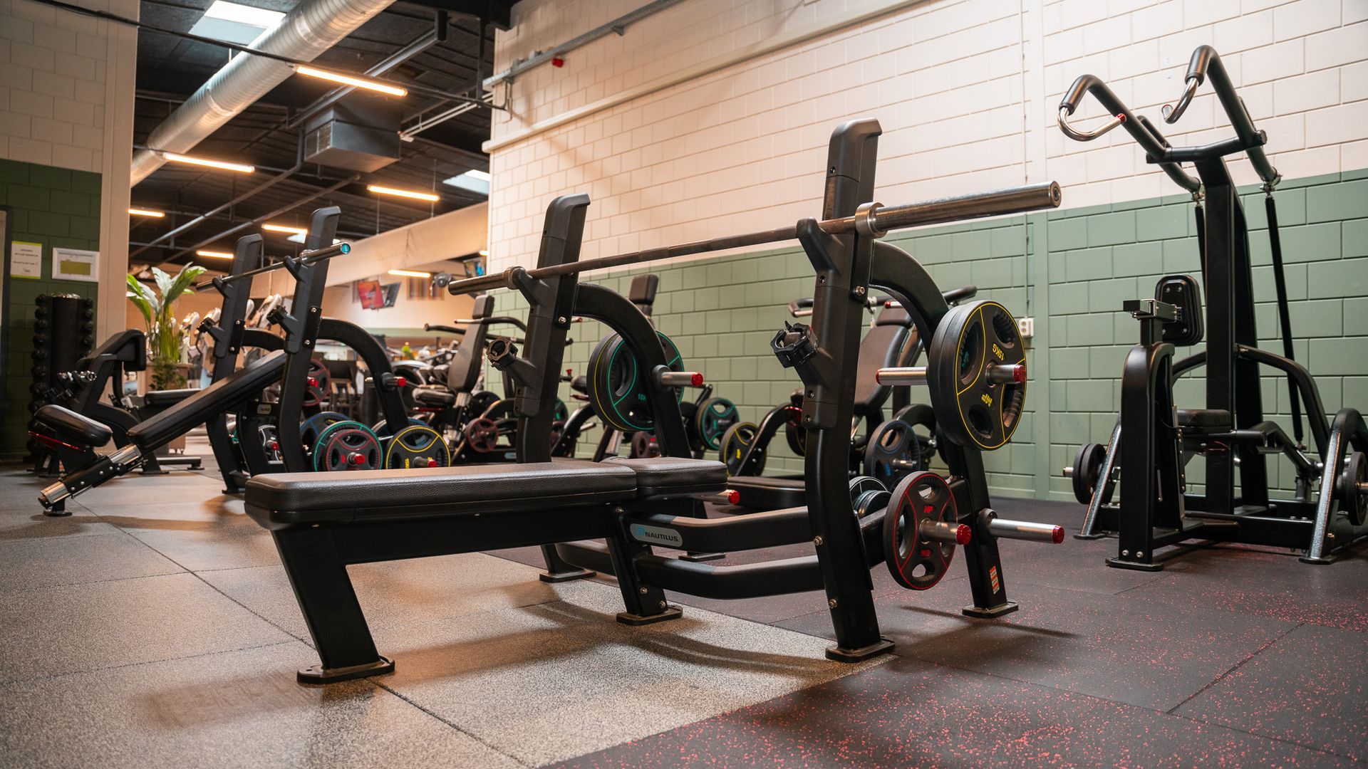 Een sportschool vol met fitnessapparatuur en een bank met een halter erop.