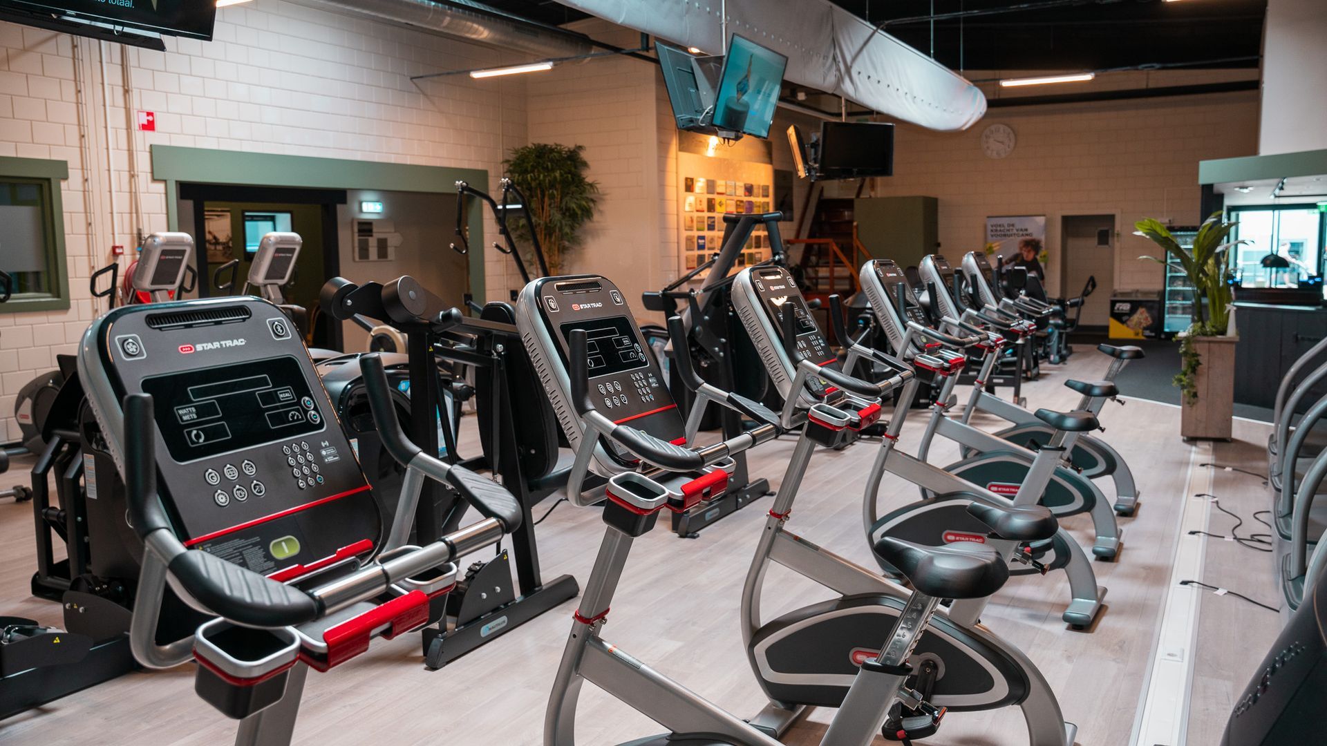 In een sportschool staat een rij hometrainers opgesteld.