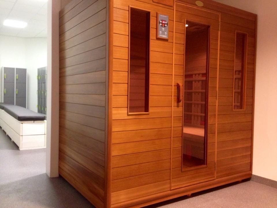 Houten sauna met glazen deur en bedieningspaneel, in een spa-achtige omgeving met een glimp van een massagetafel en kluisjes.