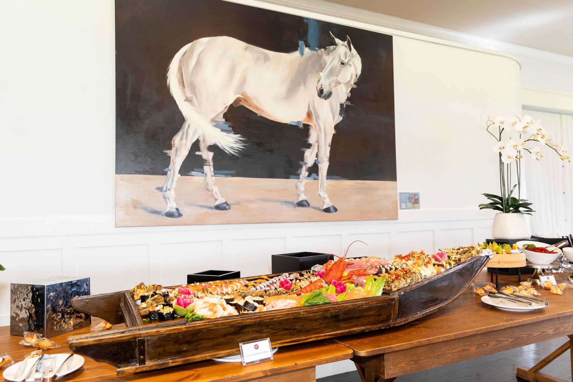There is a painting of a horse on the wall above a buffet table.