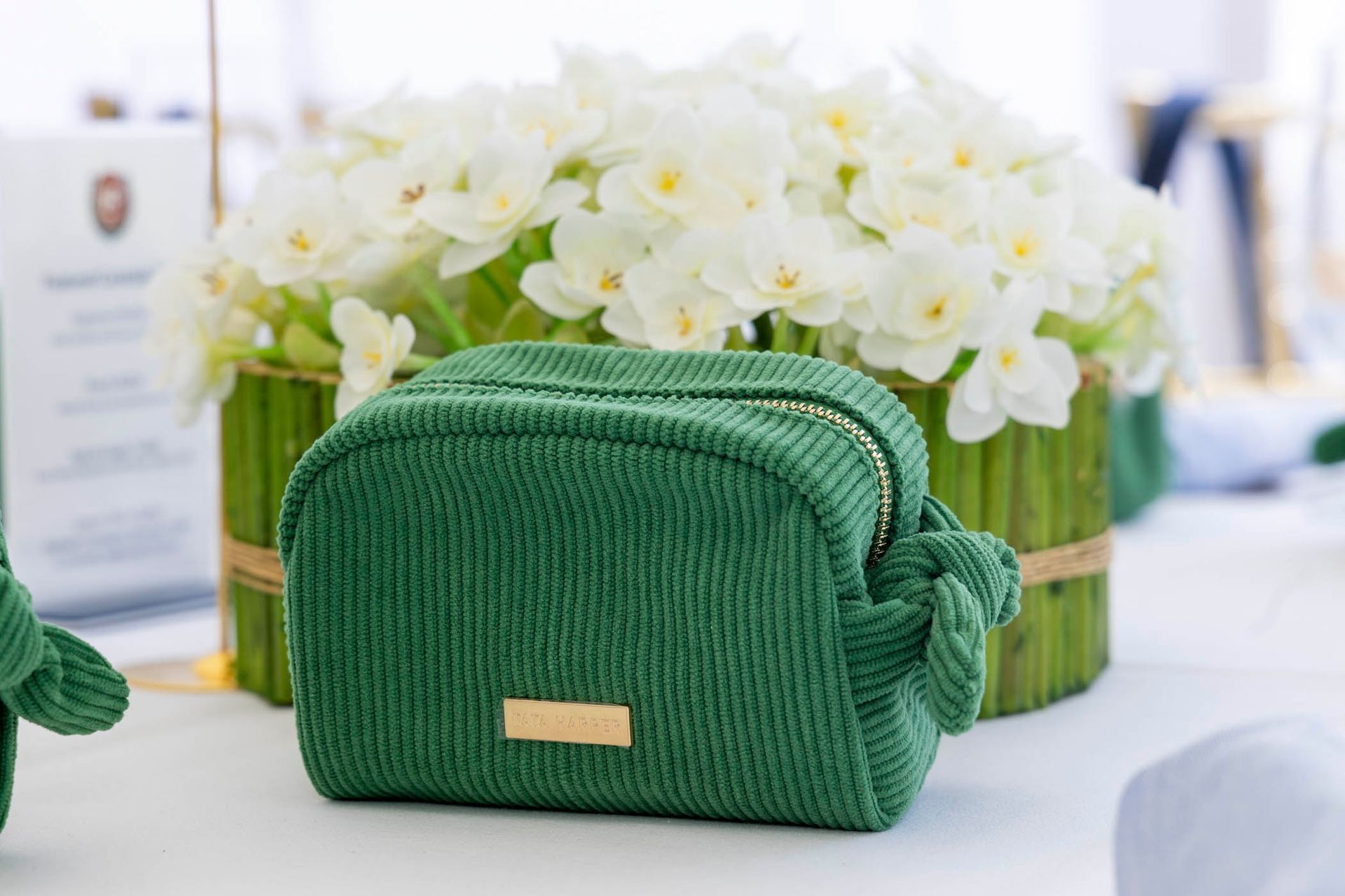 A green cosmetic bag is sitting on a table next to a vase of flowers.