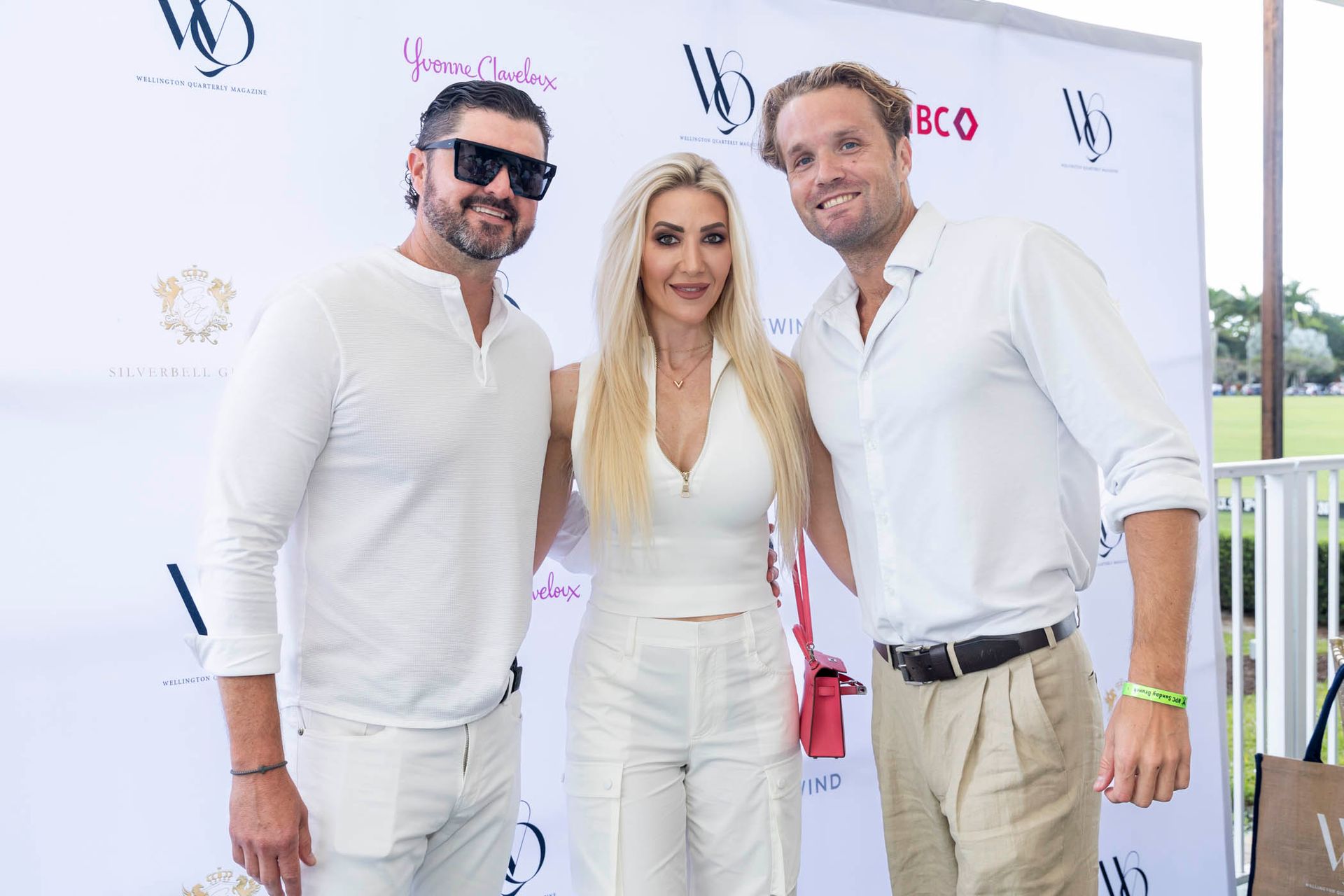 Three people are posing for a picture in front of a white wall.