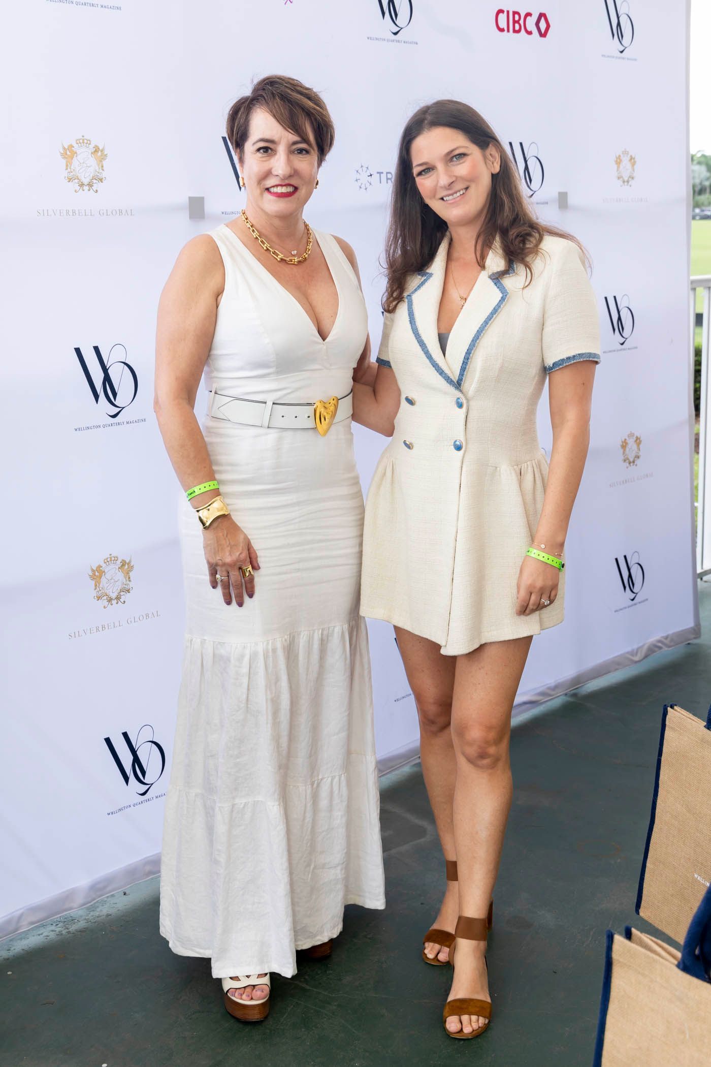 Two women in white dresses are standing next to each other in front of a white wall.